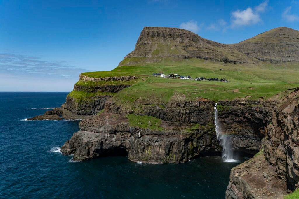 Faroe Islands – Dramatic cliffs with a waterfall tumbling into the ocean, surrounded by rugged autumn landscapes