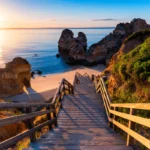 Scenic view of Praia do Camilo in Lagos, Algarve, with a wooden staircase leading to golden sands and dramatic rock formations at sunrise.
