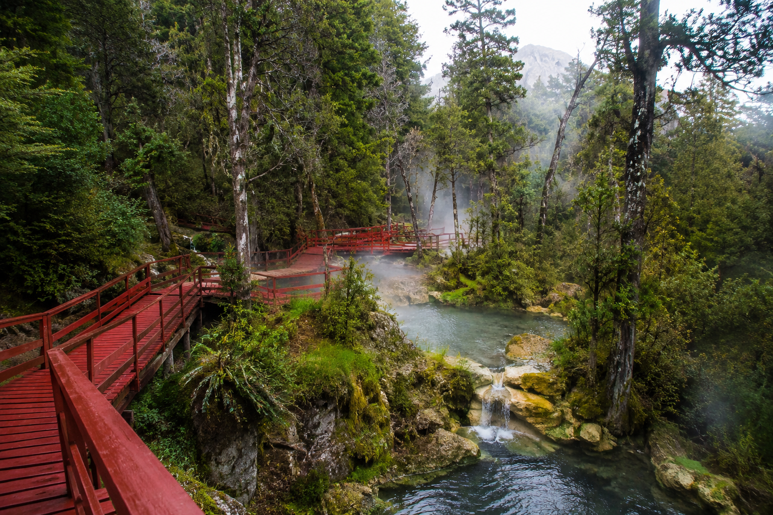 7 Best Hot Springs to Visit in October (Before the Winter Crowds Show Up) 18 Red wooden walkways leading to hot spring pools in a Chilean forest